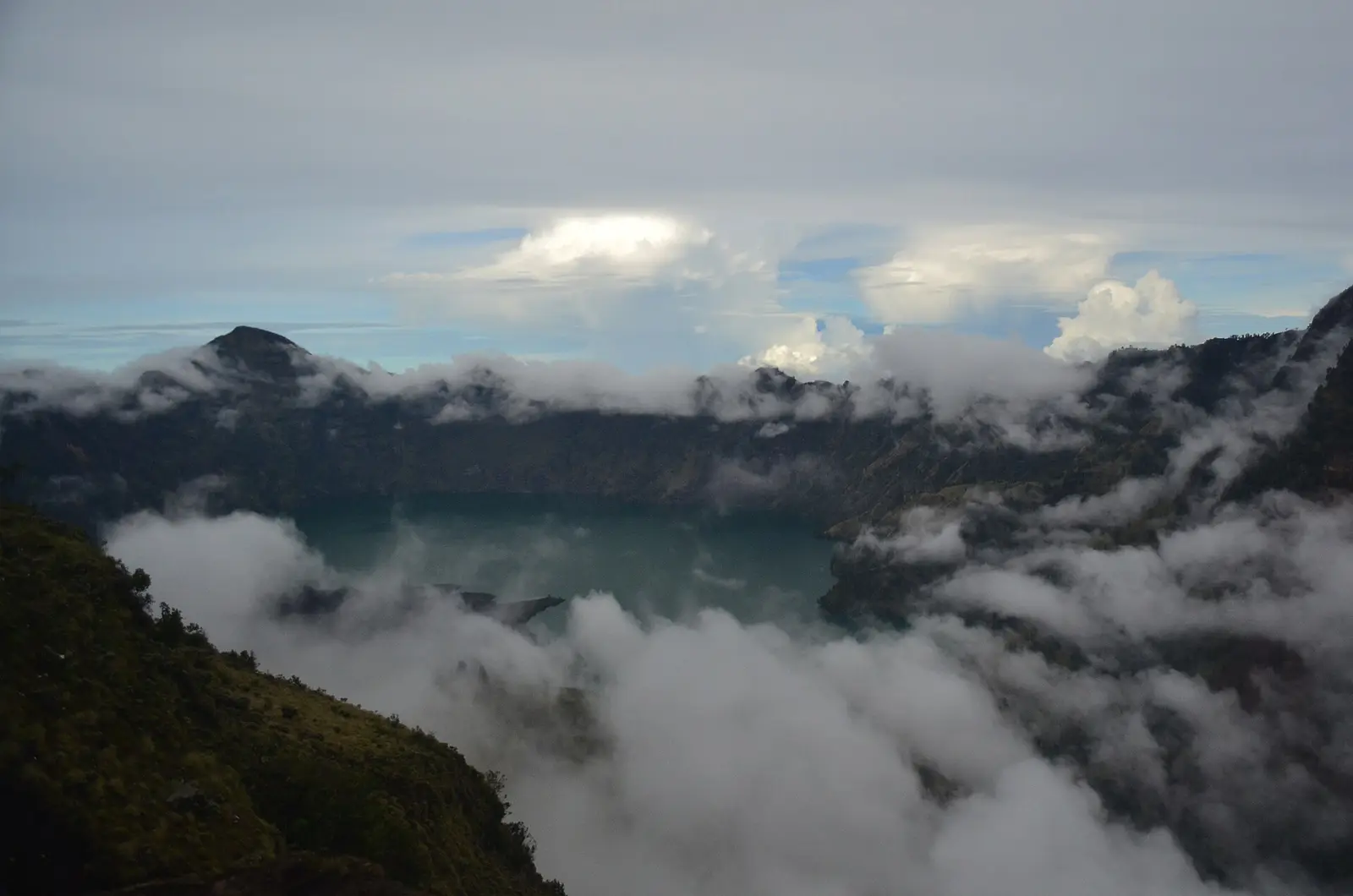 Cloud pouring over the caldera wall into the Segara Anak basin, seen from a forested rim